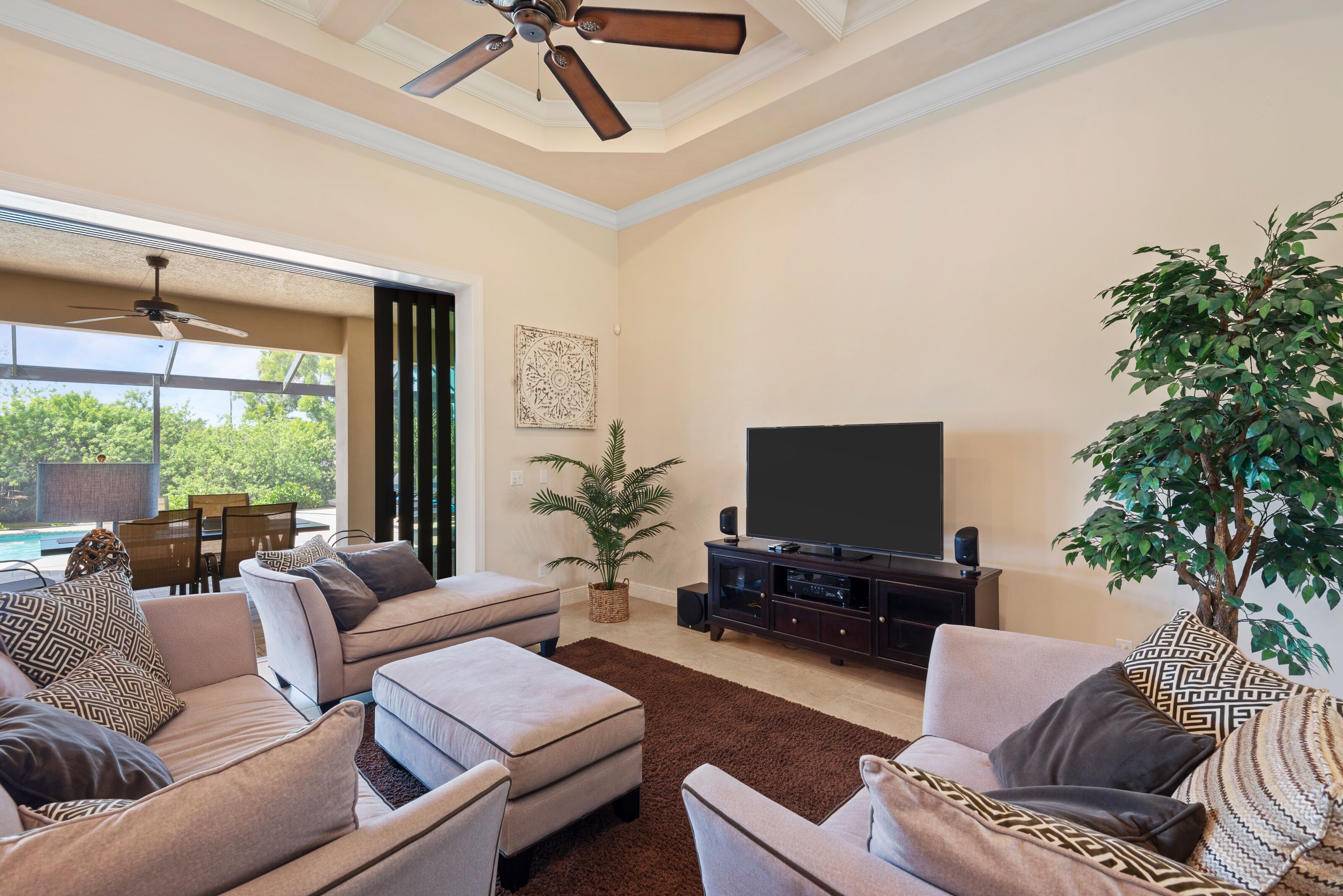 A living room with a ceiling fan, a large flat-screen TV, and a dining area with a view of the outdoors.