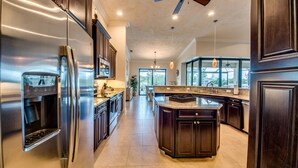 A modern kitchen with dark wood cabinets, stainless steel appliances, and a large island. - SW Cape Coral Waterfront Villa "Summerset" | Pool + Jacuzzi | south-facing | (Cape Coral)