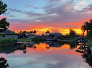 A sunset over a calm lake with buildings and palm trees in the foreground.