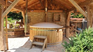 A wooden hot tub with a wooden bench and a stone wall in the background.