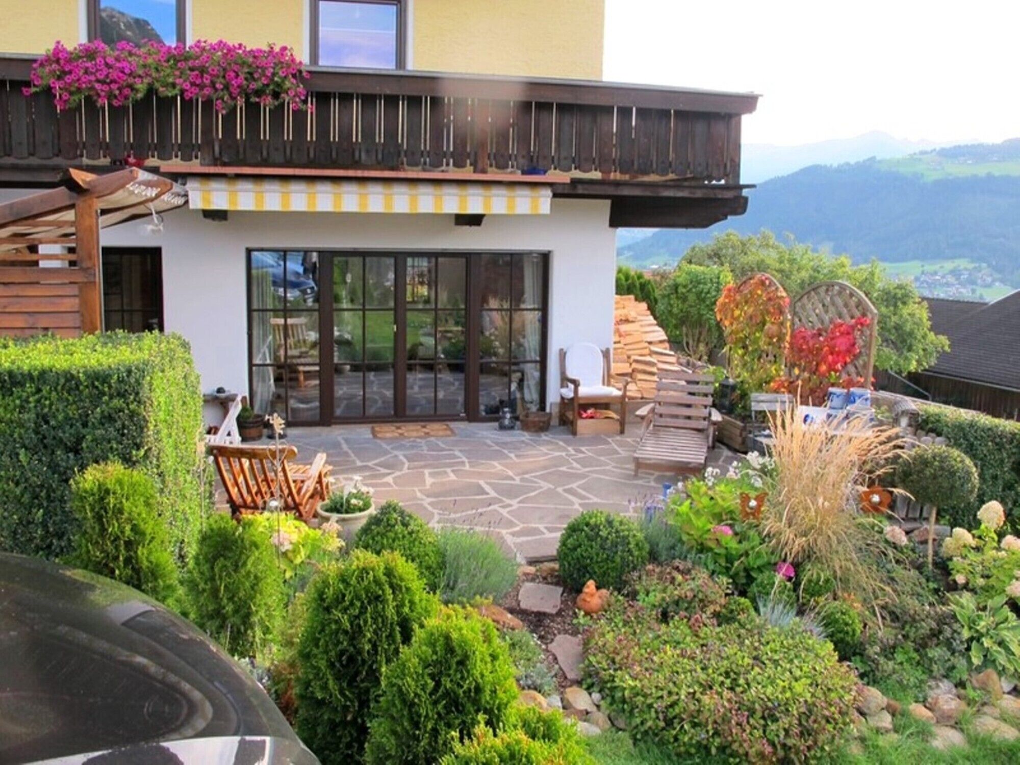 A modern house with a stone patio, wooden deck, and a variety of plants and flowers.