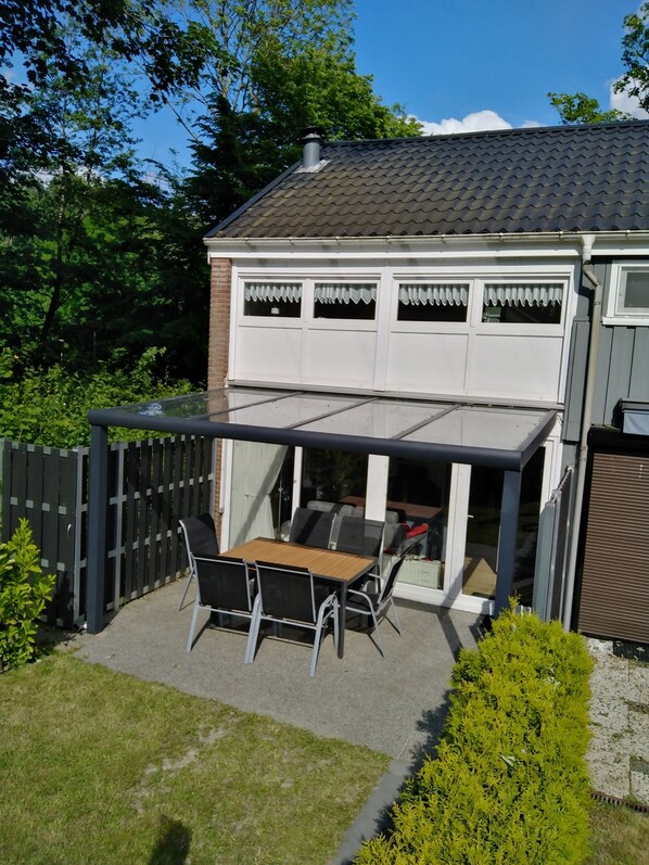 A covered patio with a table and chairs, a fenced backyard, and a house with a tiled roof.