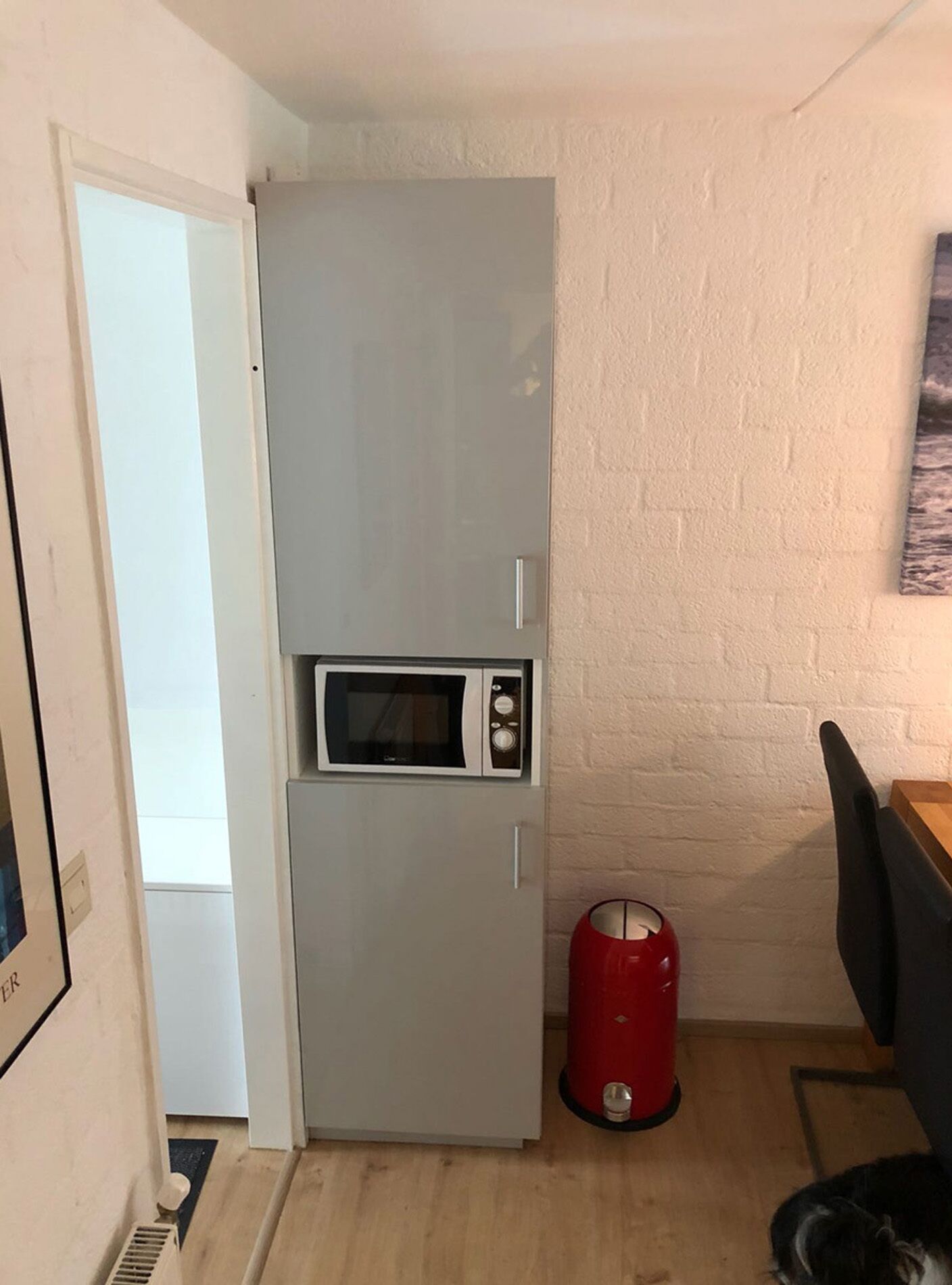 A compact kitchen with a built-in microwave and a red trash bin.