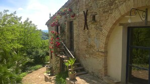 Un edificio de piedra con una escalera que conduce a una puerta, rodeado de follaje y vistas al campo.