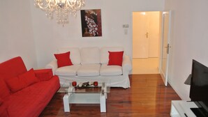 A living room with a white sofa, red cushions, a glass coffee table, a chandelier, and a painting on the wall. - Totally new apartment, central location, competitive price, WiFi, elevator (Wien)