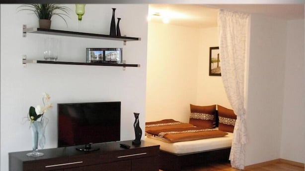 Un dormitorio con cama, televisor, cómoda y repisas con objetos decorativos.