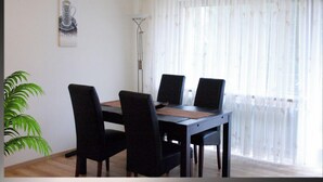 Un comedor con una mesa y cuatro sillas, una lámpara de pie y un ventanal con cortinas translúcidas.