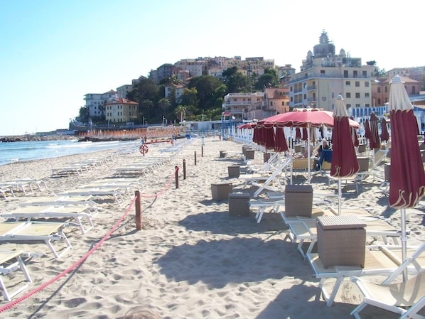 A beach with sun loungers and umbrellas, a lifeguard tower, and buildings in the background. - Stylish apartment with a beautiful garden, 5 km to the beach (Dolcedo)
