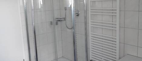 A modern bathroom with a glass-enclosed shower, a white bathtub, and a tiled floor.