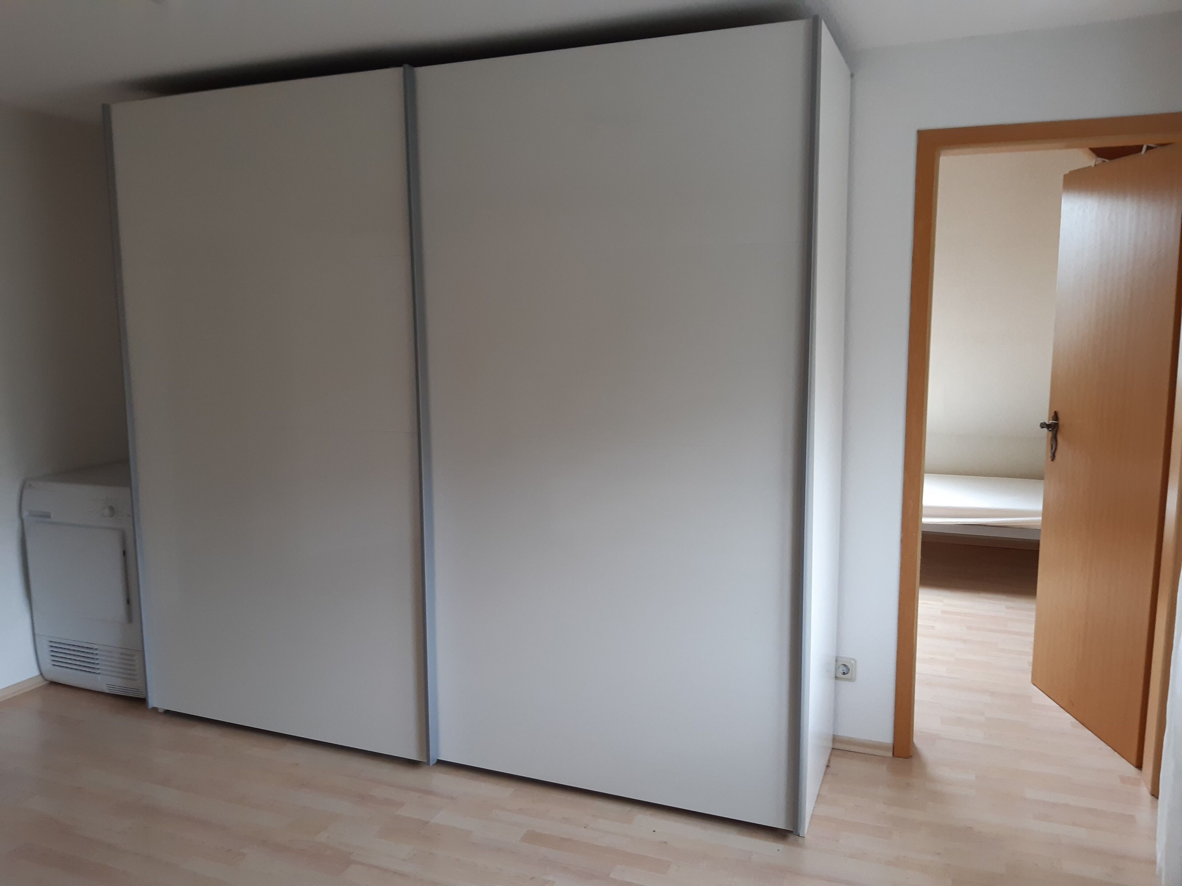 Ein Zimmer mit einem großen Kleiderschrank, einer Holztür und einem kleinen Heizgerät auf dem Boden.