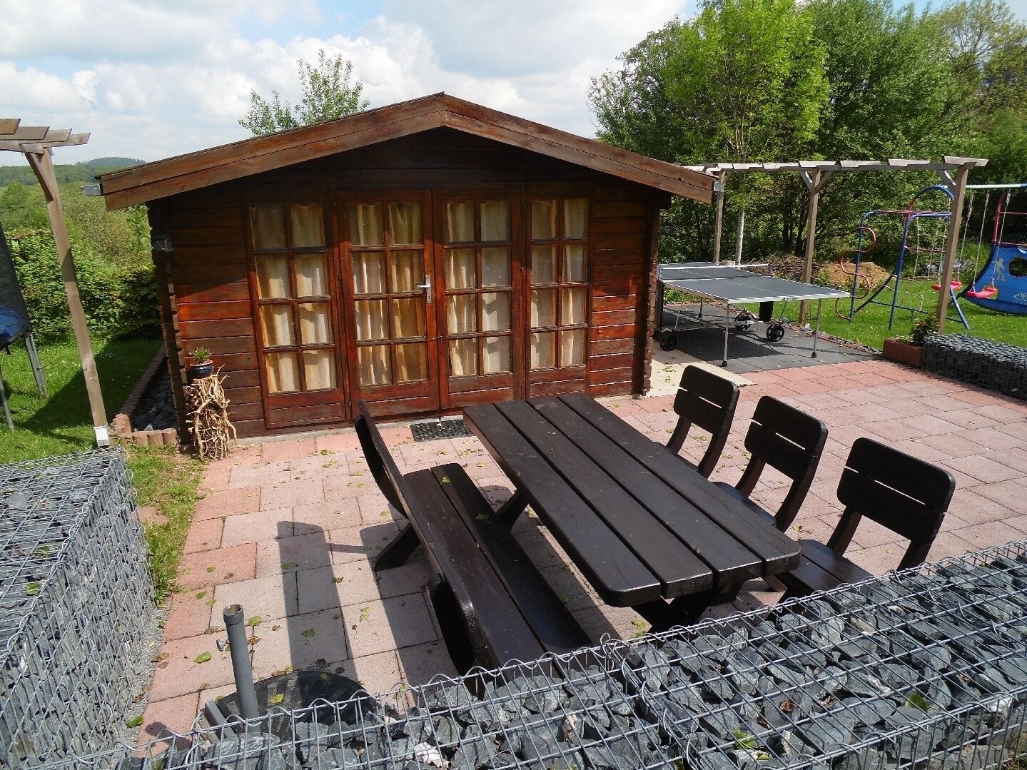 Een houten chalet met terras, tafel en stoelen.