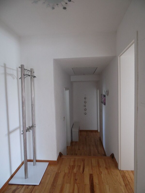 A hallway with wooden flooring, white walls, and a metal structure on the left.