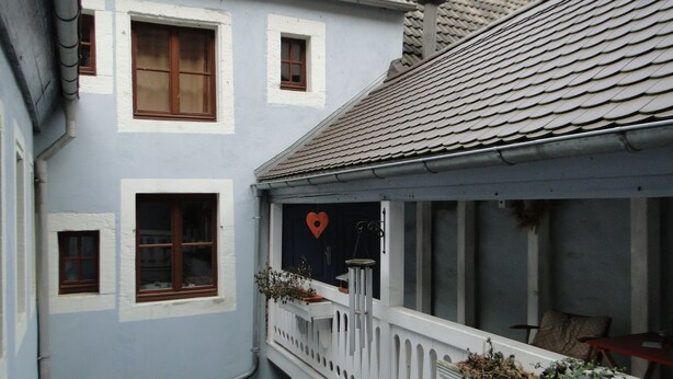 Eine schmale Straße mit einem Gebäude, das einen Balkon mit herzförmiger Dekoration und Pflanzen besitzt.