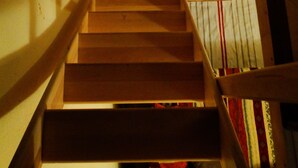 Eine Holztreppe mit Handlauf, die zu einem Raum mit einem gemusterten Vorhang führt.