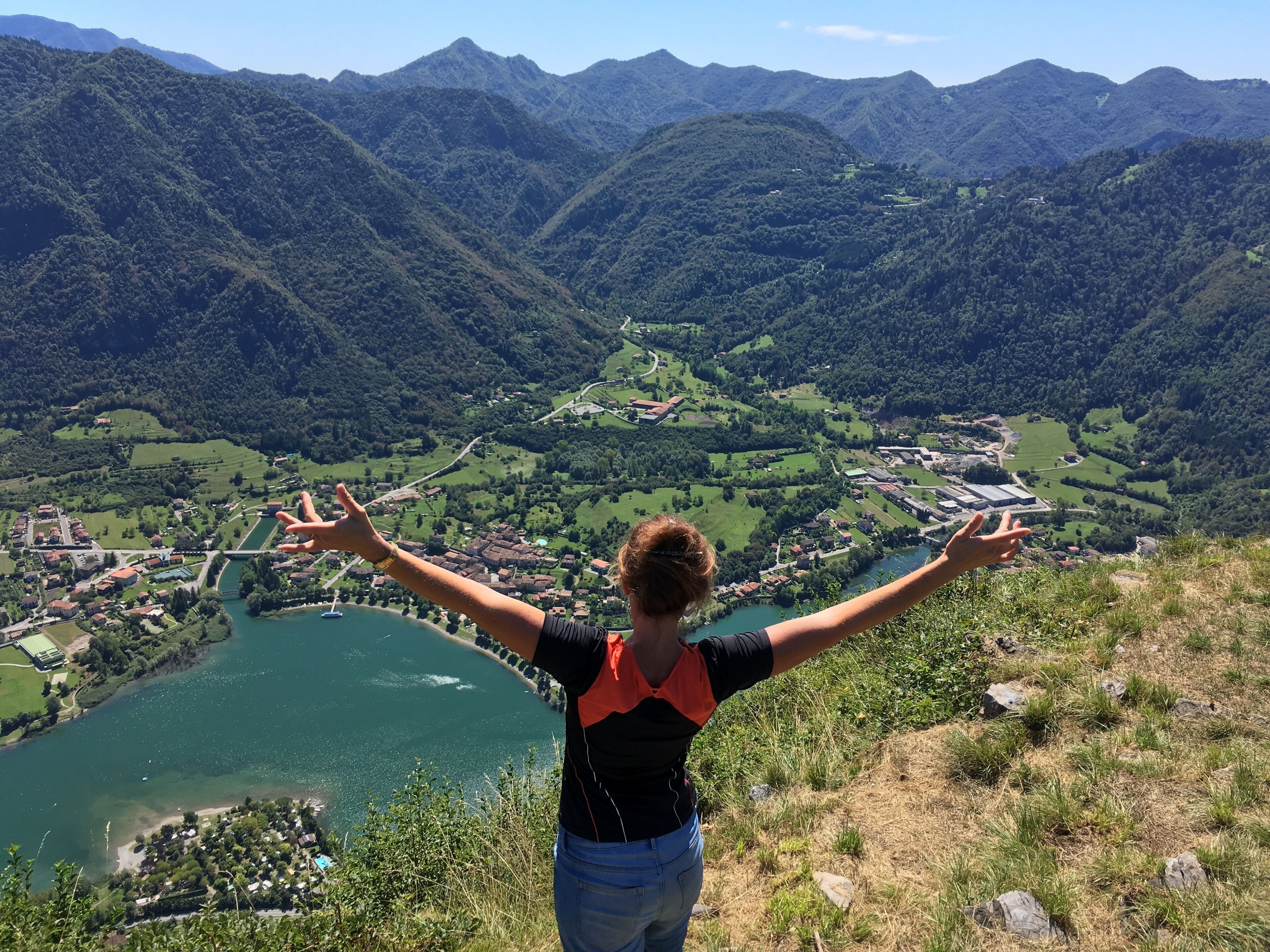 Une personne se tient sur une colline, d’où elle a une vue sur une vallée, un lac et des bâtiments.
