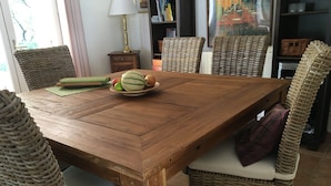 Ein Holztisch mit gewebten Stühlen, eine Fruchtschale und eine Lampe in einem Raum mit Bücherregalen und einem Gemälde.