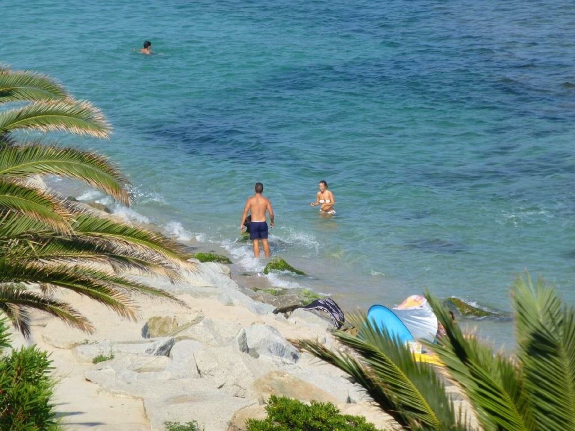 Une plage avec une eau cristalline, des gens qui se baignent et une planche de surf sur le sable.