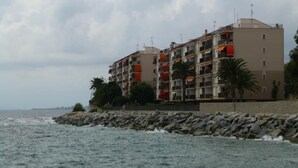 Un edificio costero con varios balcones, un litoral rocoso y palmeras.
