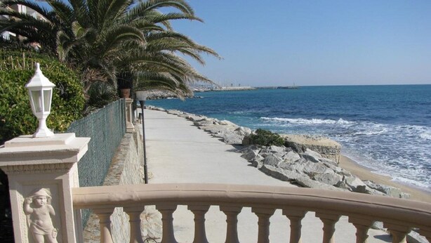Un paseo marítimo con barandilla, palmeras y vista al mar.