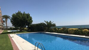 Una piscina rectangular con agua azul cristalina, rodeada por un deck pavimentado y una zona verde.