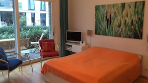 A hotel room with a bed, a TV, a desk, and a chair. There is a balcony with a view of buildings and greenery. - Luxury apartment in the trendy district of Berlin Mitte (Berlin)
