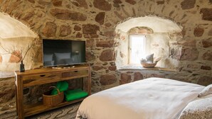 Ein Zimmer mit Stehwänden, einem Bett, einem Holzkonsolentisch mit Fernseher und einem Fenster mit Korb auf der Fensterbank.