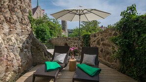 Eine Terrasse mit zwei Korbstühlen, einem Holztisch und einem großen Sonnenschirm.