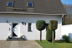 A modern house with a white exterior, a tiled roof, and a front door with a small window above it. There are two potted plants on the steps leading to the door.
