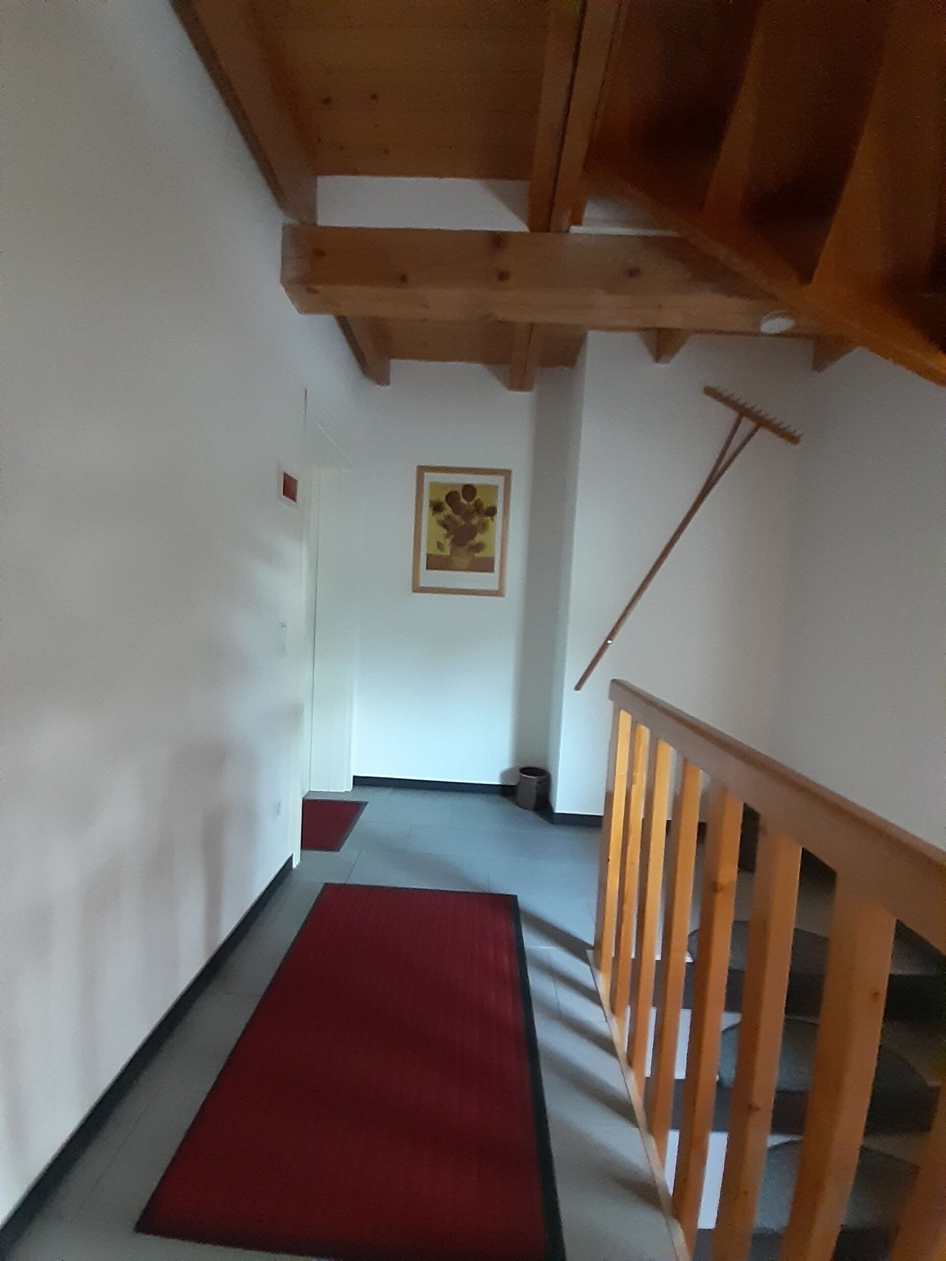 Ein Flur mit einer Holztreppe, einer roten Matte auf dem Boden und einem gerahmten Bild an der Wand.