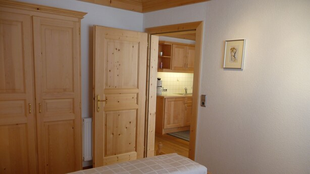 A bedroom with two beds, wooden wardrobes, a kitchen visible through an open door, and a framed picture on the wall.