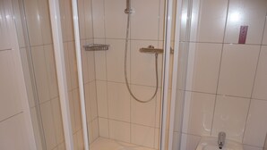 A bathroom with a glass-enclosed shower, a pedestal sink, and tiled walls.