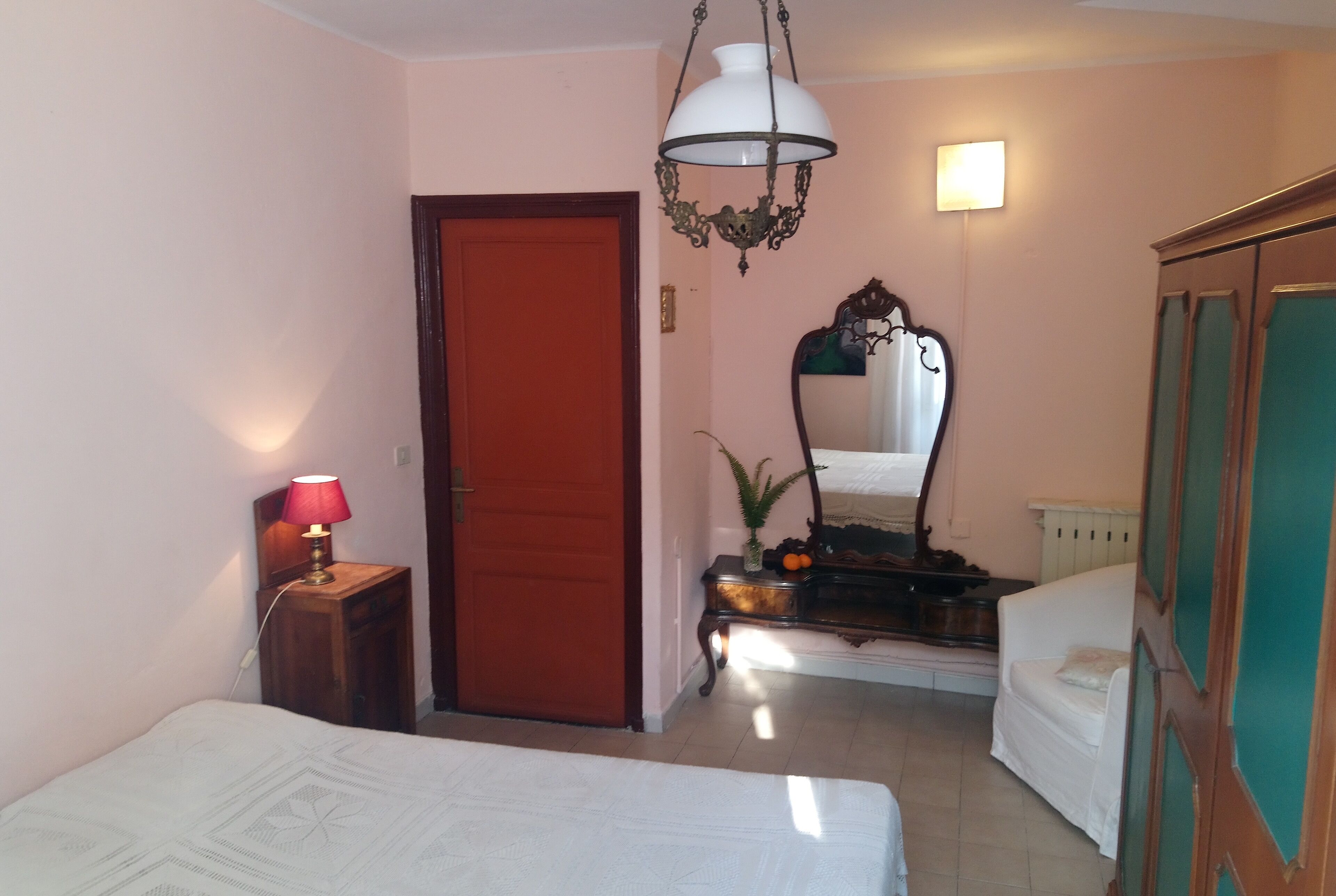 Quarto com cama, mesa de cabeceira com abajur, cômoda, espelho e porta.