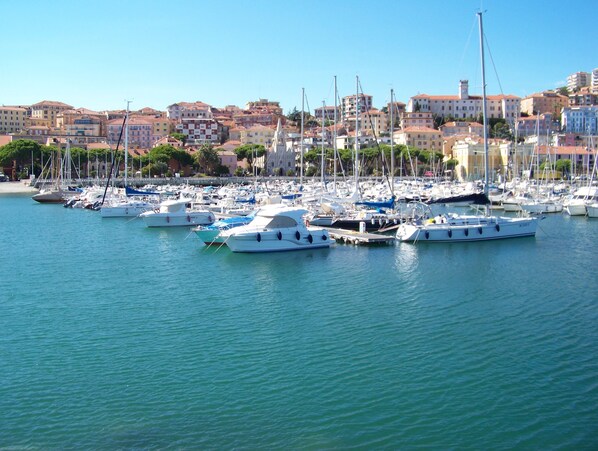Eine Marina mit vielen vertäuten Booten, umgeben von Gebäuden mit roten Dächern und wolkenlosem, blauem Himmel.