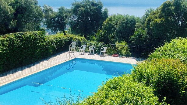 A rectangular swimming pool with a clear blue water surface, surrounded by lush greenery and trees. - Apartment with air conditioning, sea view, swimming pool, Wi-Fi, quiet hill, parking. (Toscolano Maderno)