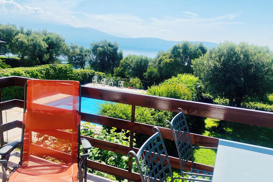 A terrace with a view of a lake and mountains, featuring a table and chairs.