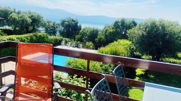 A terrace with a view of a lake and mountains, featuring a table and chairs.