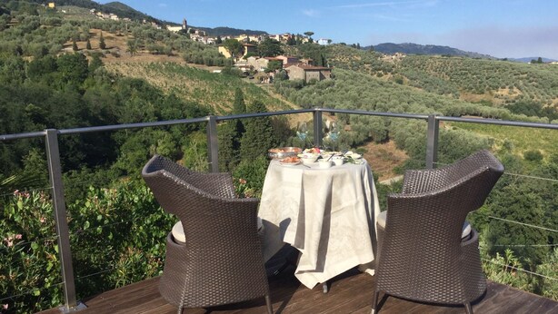 Eine Terrasse mit Korbstühlen und einem Esstisch, mit Blick auf ein Hügeldorf.