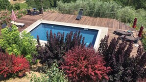 Ein rechteckiger Pool mit umlaufender Holzterrasse, ausgestattet mit Liegestühlen und Sonnenschirmen.