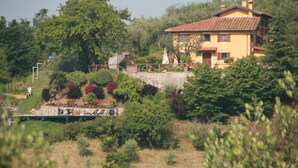 Ein gelbes Haus mit rotem Dach, umgeben von viel Grün und einer kleinen Brücke.
