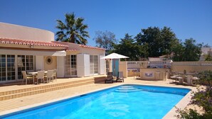 Ein Schwimmbecken mit gefliestem Sonnendeck, Sitzgelegenheiten im Freien und Palmen im Hintergrund.