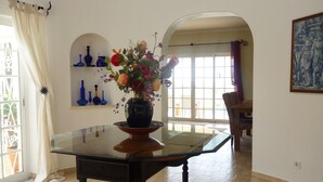 Ein Essbereich mit einem Glastisch, einer Blumenvase und blauen Vasen auf Regalen.