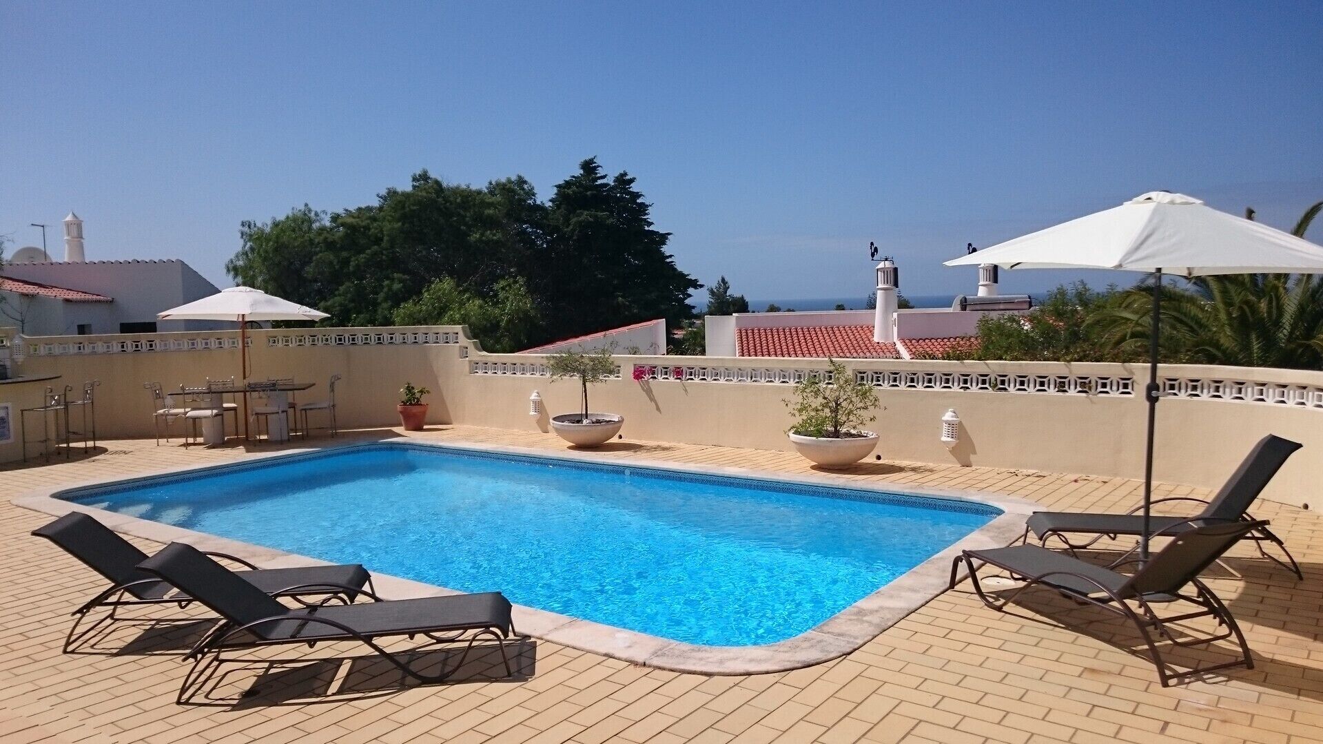 Une piscine rectangulaire, bordée d’une terrasse carrelée, entourée de chaises longues et de parasols.
