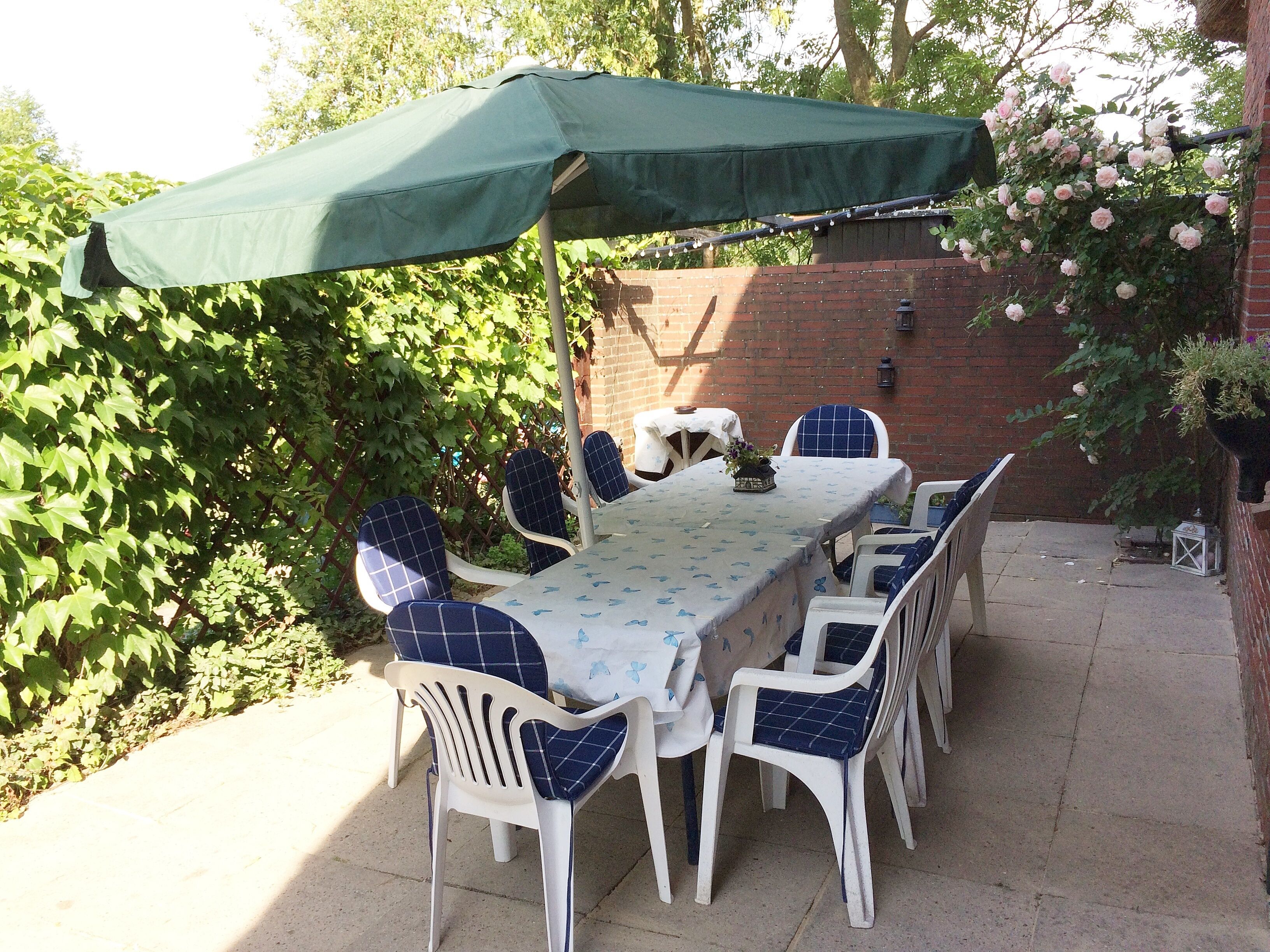An outdoor patio with a table and chairs, a green umbrella, and a brick wall.