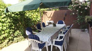An outdoor patio with a table and chairs, a green umbrella, and a brick wall.