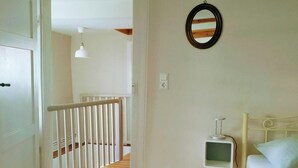 Ein Schlafzimmer mit einem weißen Bett, einem kleinen Nachttisch, einem Spiegel an der Wand und Holzböden.