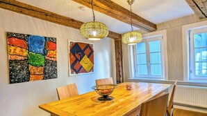 Ein Essbereich mit einem Holztisch, Stühlen, hängenden Pendelleuchten und Kunstwerken an den Wänden.