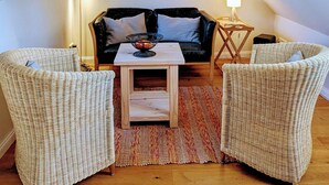 Ein gemütliches Schlafzimmer im Loft-Stil mit schrägen Wänden, einer schwarzen Leder-Couch, zwei Korbsesseln, einem kleinen Holztisch und einer Stehlampe.