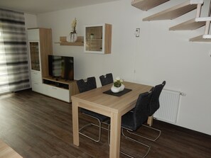 A modern living room with a wooden dining table, chairs, a TV, and a fireplace.