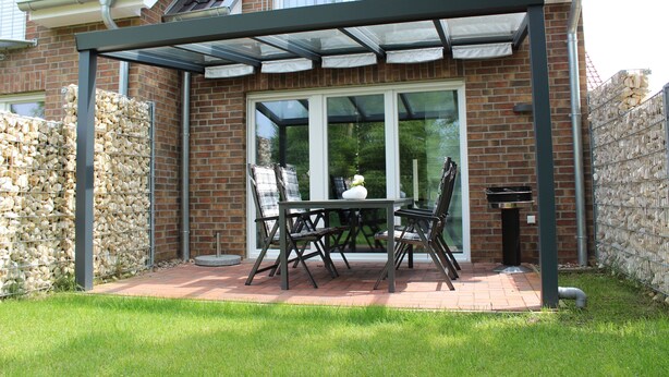 A covered patio with a table and chairs, a glass door, and a stone wall. - TOP!!! Headquarters u. quiet location, modern DHH, garden, 5 * level, WiFi, bicycles (Horumersiel)