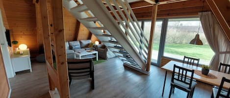 A cozy loft-style room with a wooden staircase, a dining area, and a sofa set.